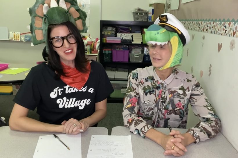Keri and a collaborator wearing playful dinosaur hats at a work table.