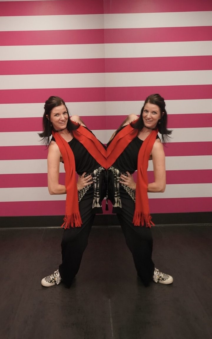 Keri in a playful dance pose against a striped wall.