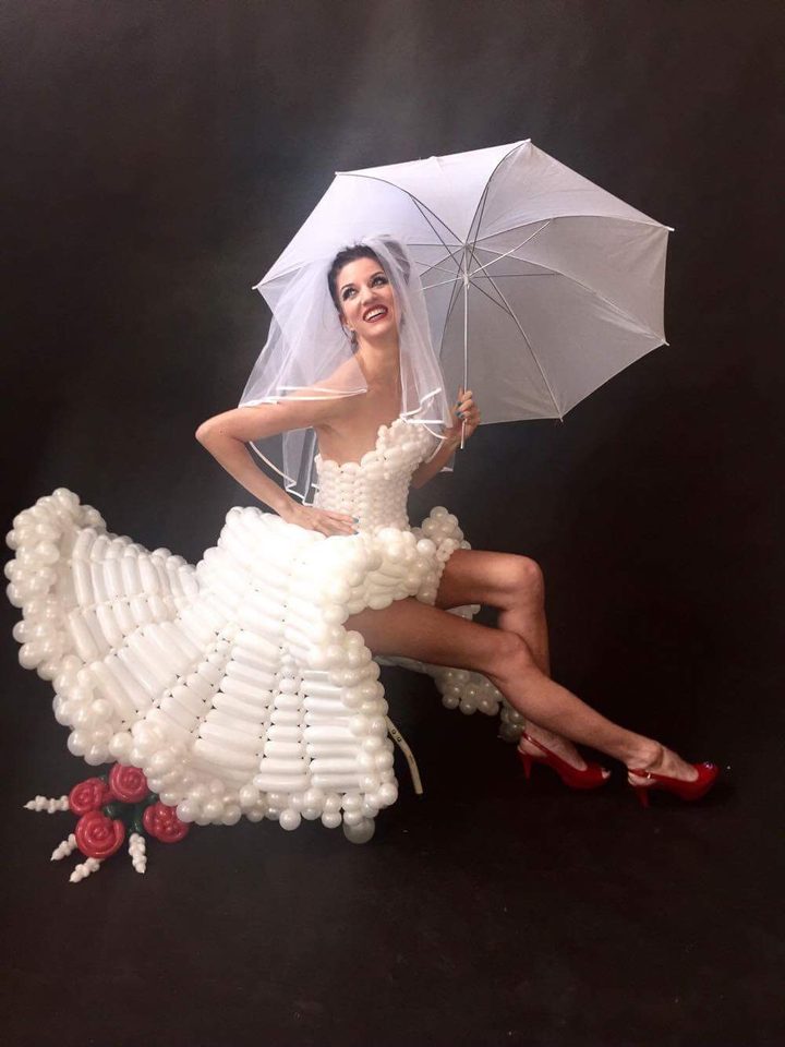 Keri in a wedding gown made entirely of balloons, holding a parasol.