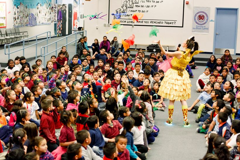 Keri in a yellow fairy costume performing for a large crowd of children.