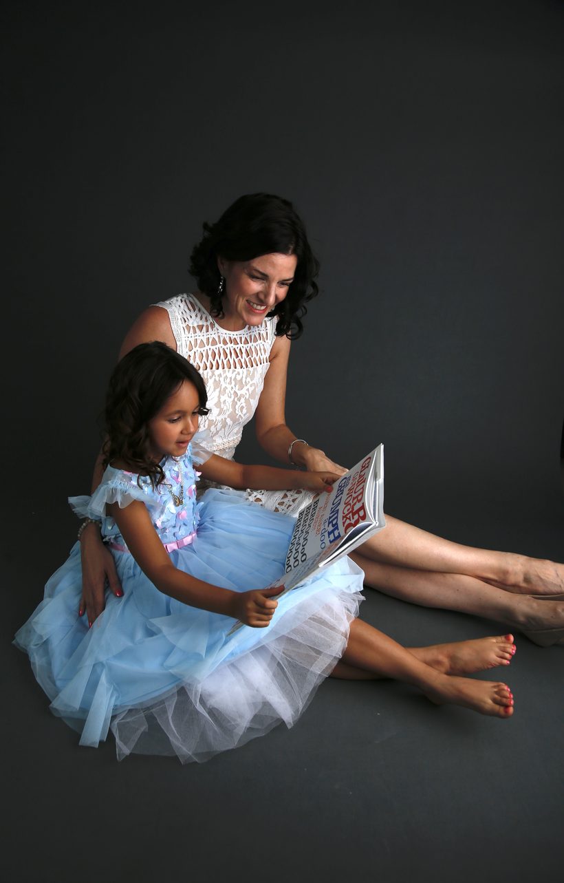 Keri reading a colorful picture book with a young child in a tutu.
