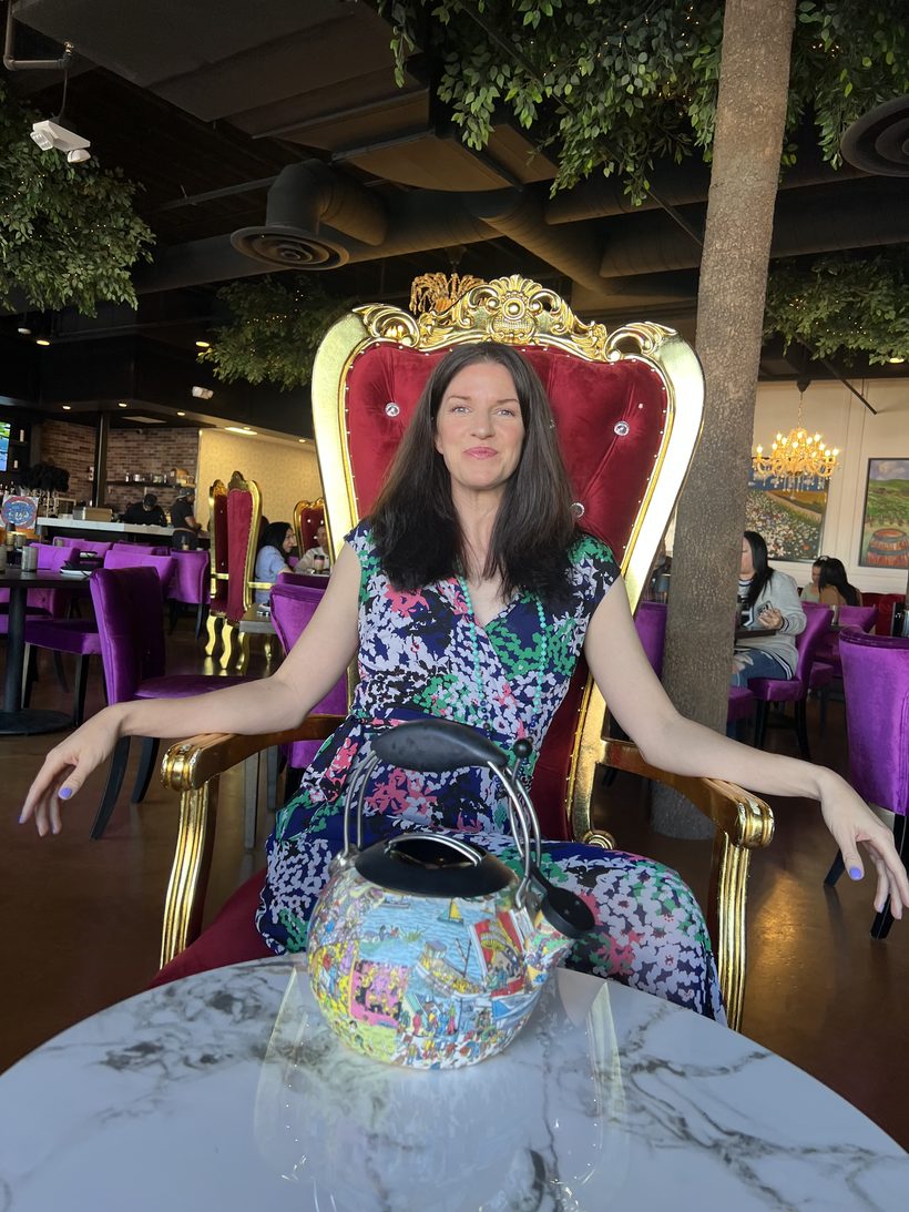 Keri seated on a golden throne chair with her signature teapot on the table.