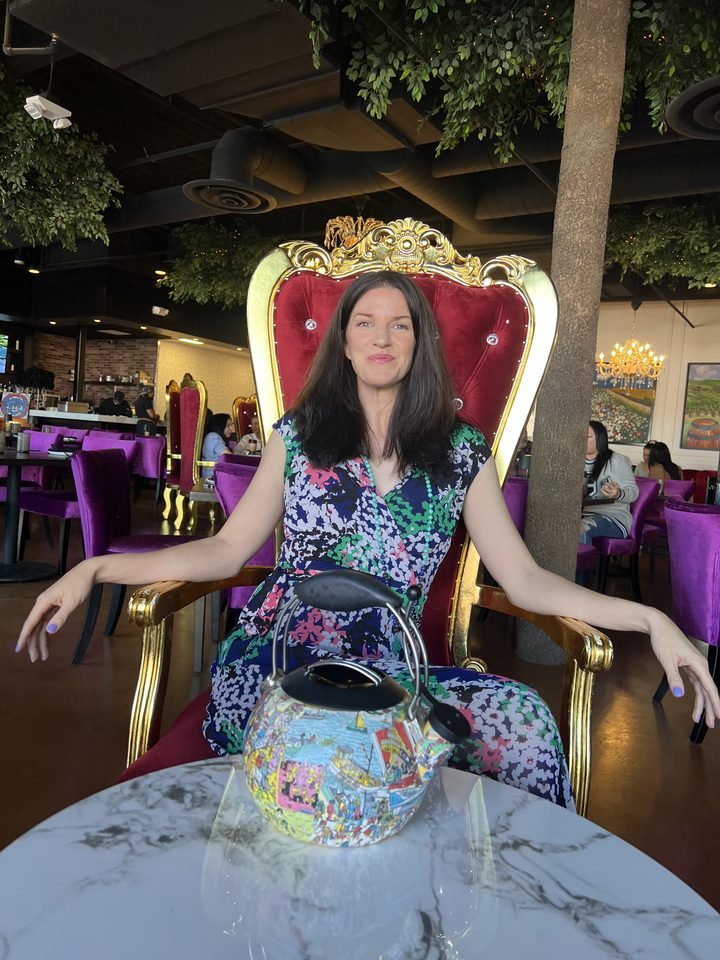 Keri seated on an ornate golden throne chair with her teapot, smiling.