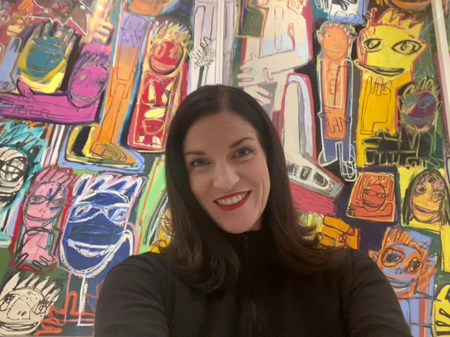Keri smiling in front of a colorful mural of painted faces.