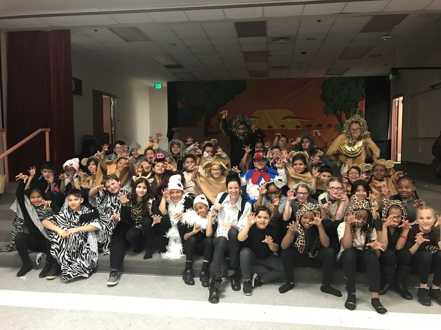 Keri with a large cast of children in animal costumes on stage.